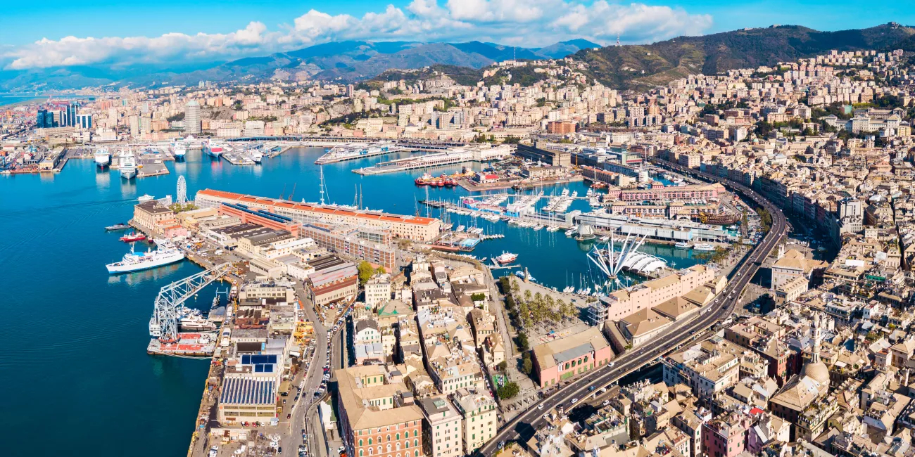 View of the port in Genoa with ships, harbor infrastructure, and the city skyline in the background