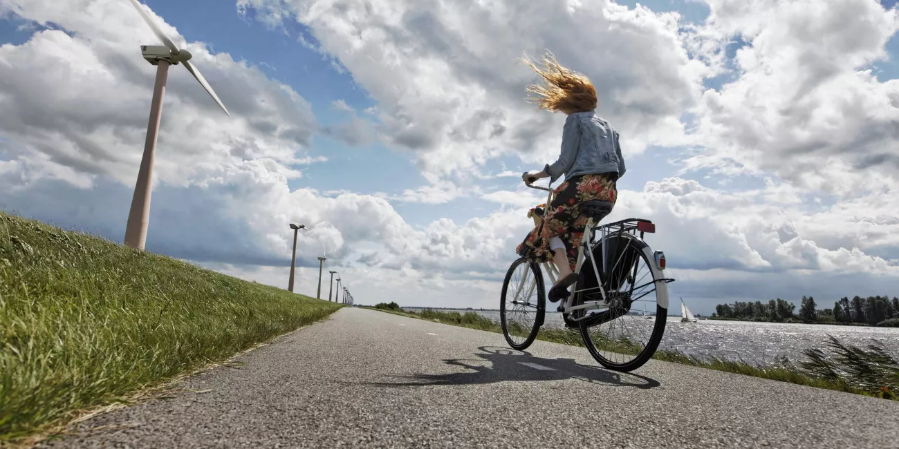young woman on her bicycle traveling on a wind blown dike in Holland, wind turbines in the background