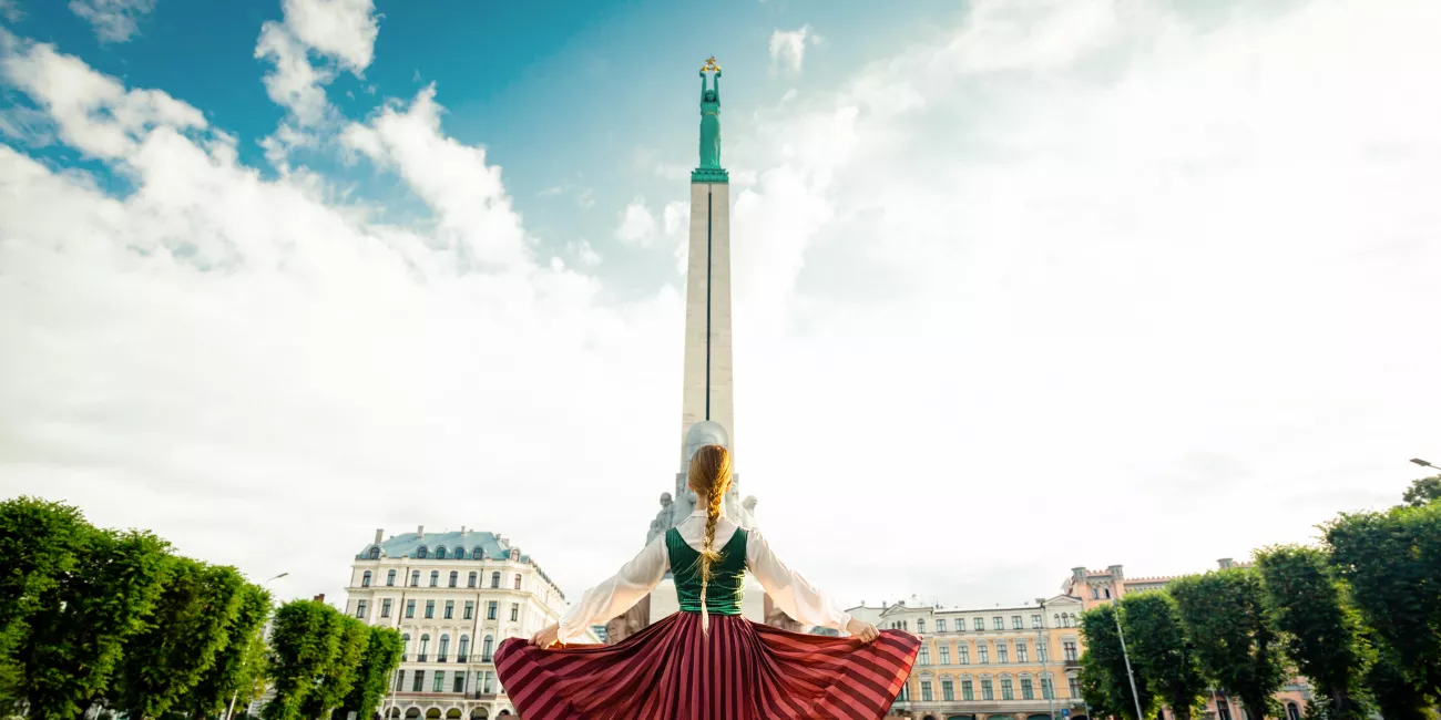 Girl in a Latvian clothes standing in front of monument of freedom