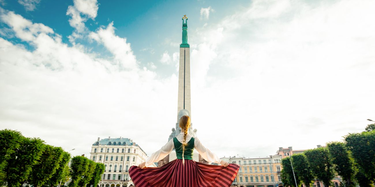 Girl in a Latvian clothes standing in front of monument of freedom