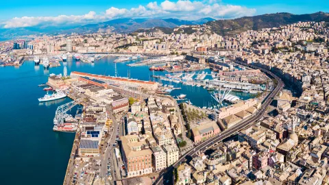 View of the port in Genoa with ships, harbor infrastructure, and the city skyline in the background
