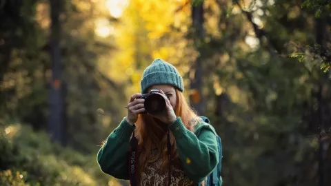 A young woman taking photos with a camera in an autumn forest