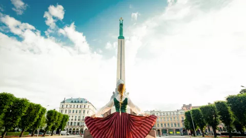 Girl in a Latvian clothes standing in front of monument of freedom