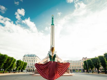 Girl in a Latvian clothes standing in front of monument of freedom
